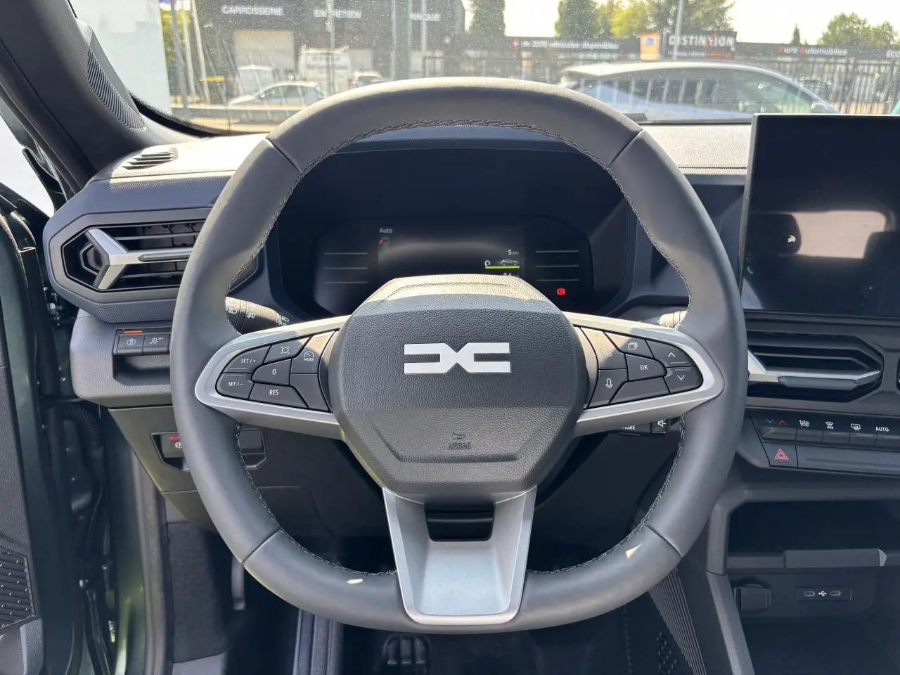 Volant noir du Dacia Duster 2025 vu de face, avec commandes intégrées et tableau de bord digital en arrière-plan.