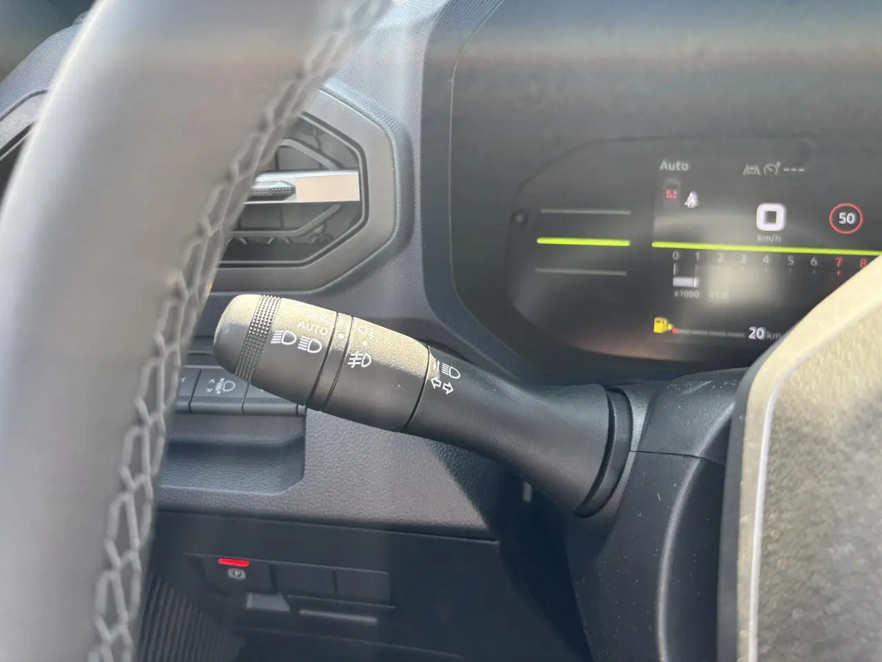 Gros plan sur la manette des feux et clignotants à gauche du volant dans le tableau de bord digital du Dacia Duster 2025.