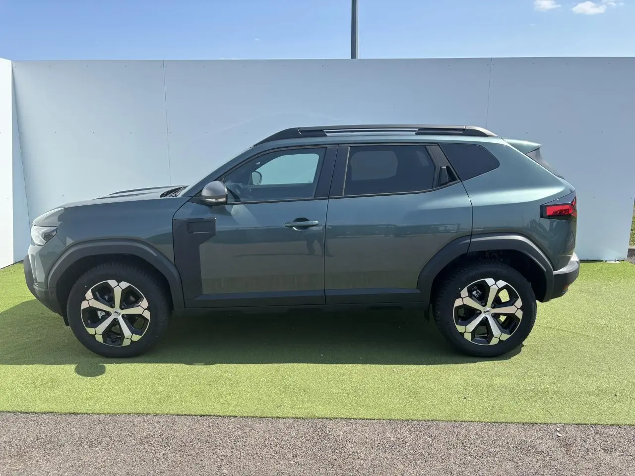Profil côté gauche du Dacia Duster 2025 vert cèdre métallisé avec jantes alliage 18 pouces diamantées.