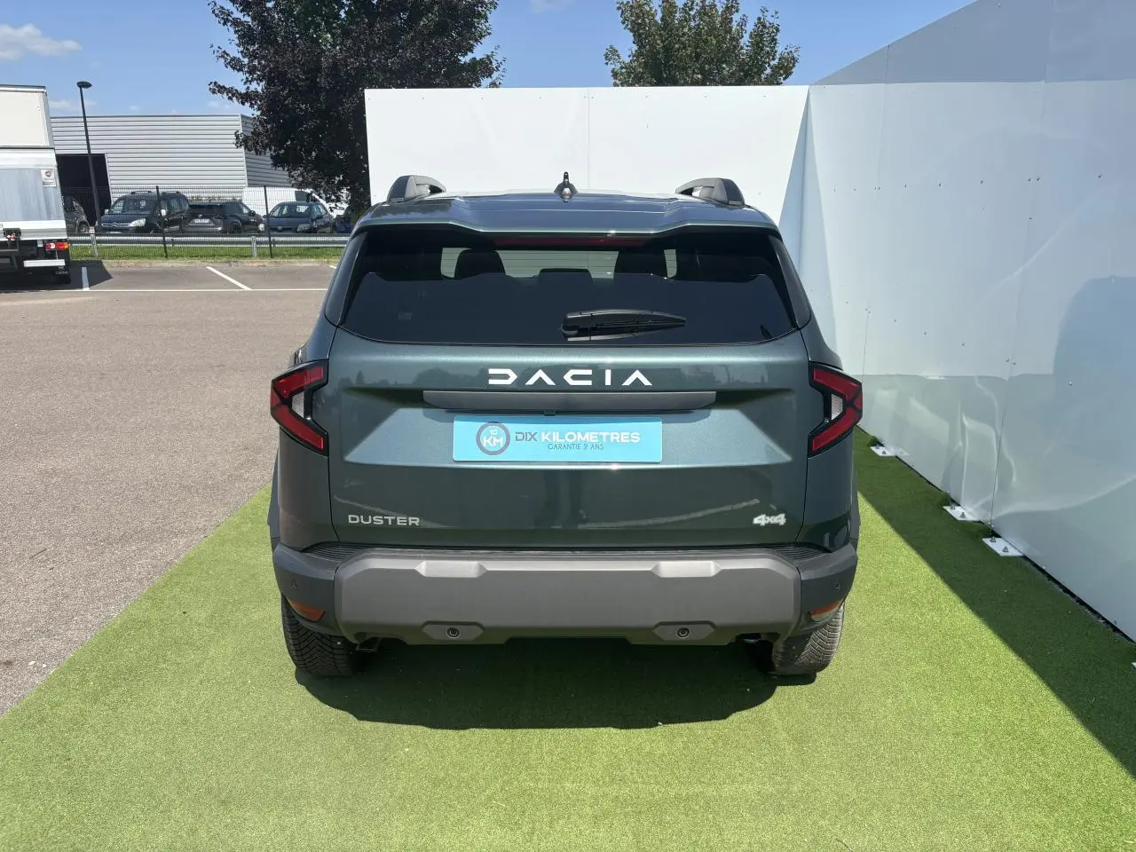 Vue arrière du Dacia Duster III vert cèdre métallisé avec logo DACIA blanc et feux arrière en forme de flèche.