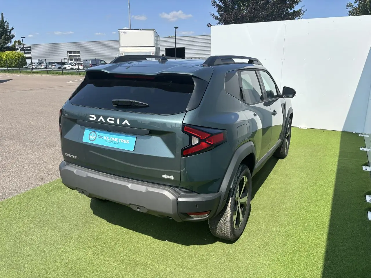 Vue 3/4 arrière droite du Dacia Duster 2025 vert cèdre métallisé avec jantes alliage et barres de toit.