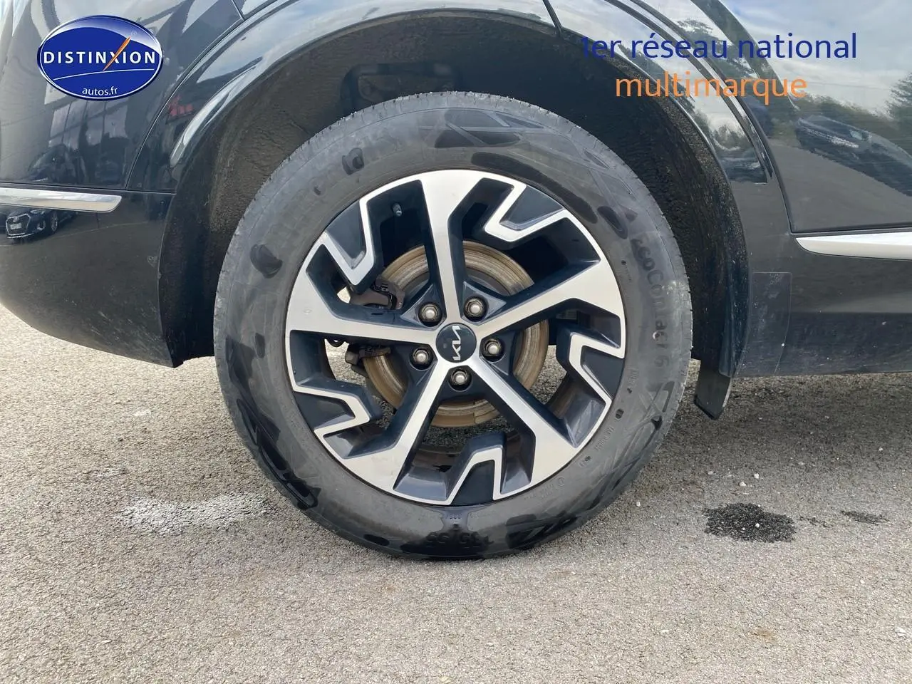 Gros plan sur la roue avant gauche noire du Kia Sportage 2023 avec jante alu bicolore au design moderne.