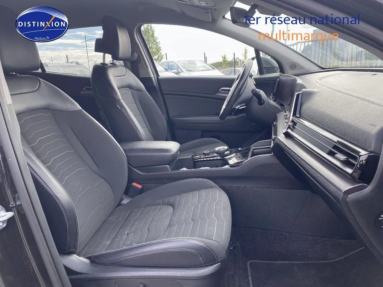 Intérieur avant du KIA SPORTAGE 2023 noir, sièges tissu noir, console centrale avec écran tactile et volant multifonction.