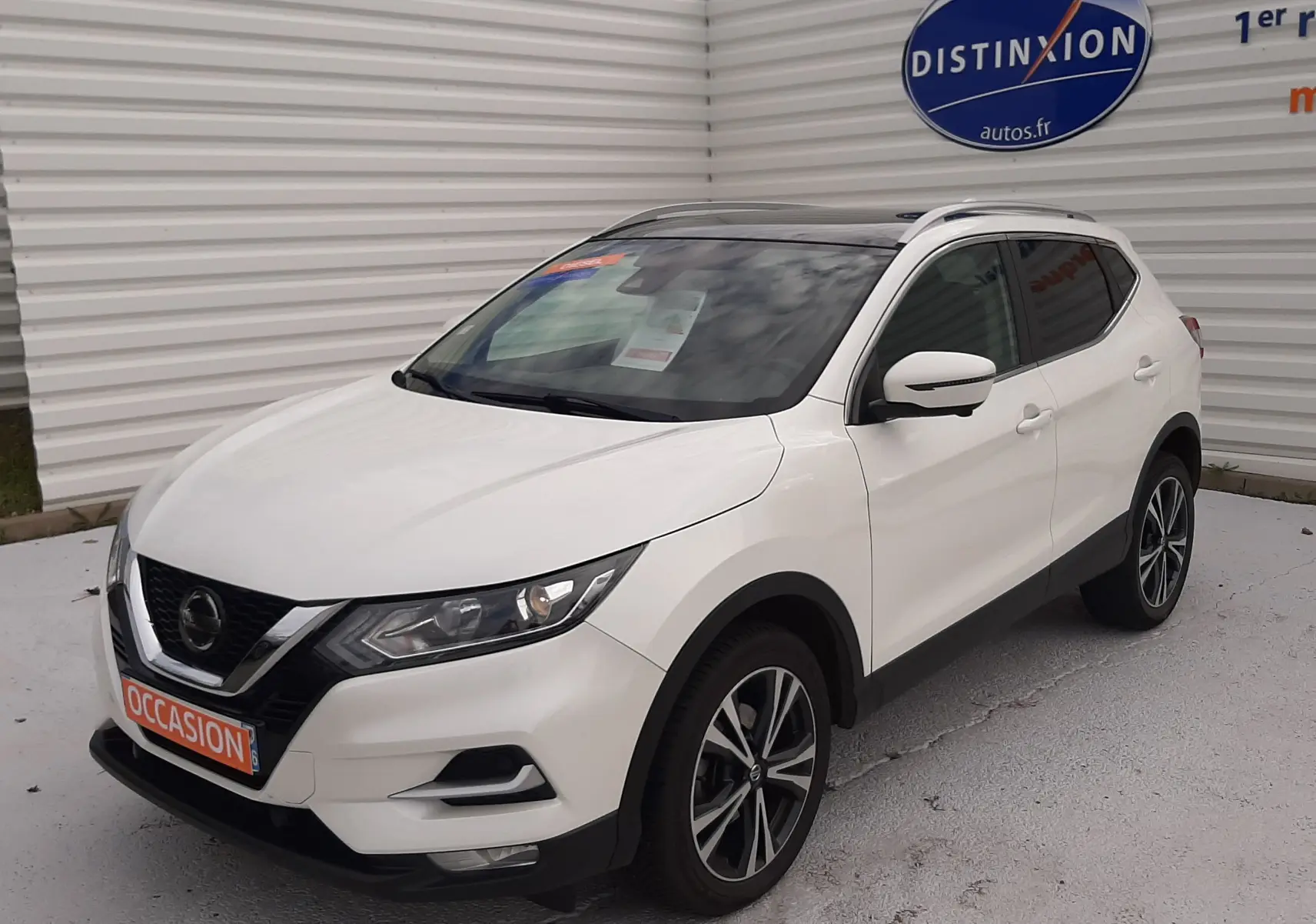Nissan Qashqai blanc en 3/4 avant droit, toit noir, jantes alliage bicolores et calandre V-Motion distinctive.
