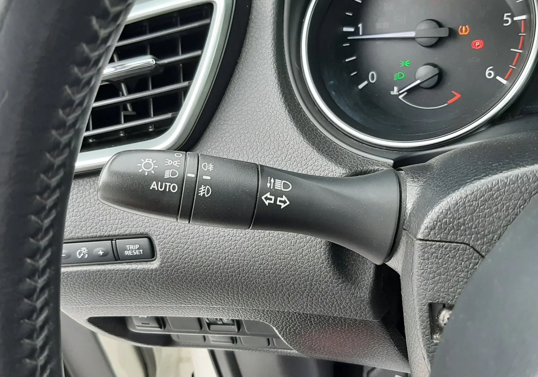 Gros plan sur la commande des feux et clignotants à gauche du volant dans l'habitacle noir du Nissan Qashqai blanc 2020.