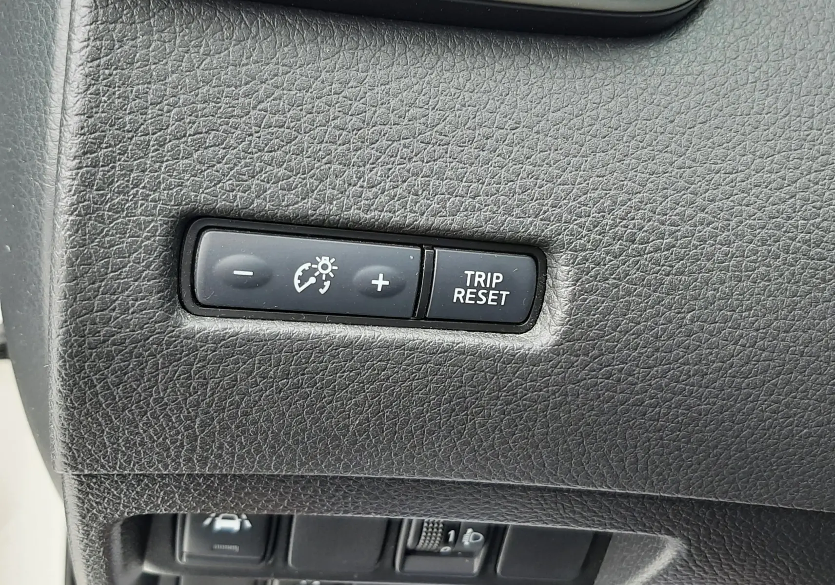 Détail du tableau de bord noir du Nissan Qashqai 2020, avec boutons de réglage d'éclairage et reset du compteur.