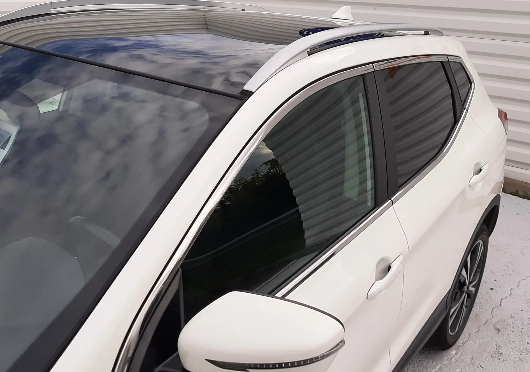 Vue 3/4 avant droit du Nissan Qashqai blanc 2020 avec toit panoramique et rétroviseur latéral intégré.