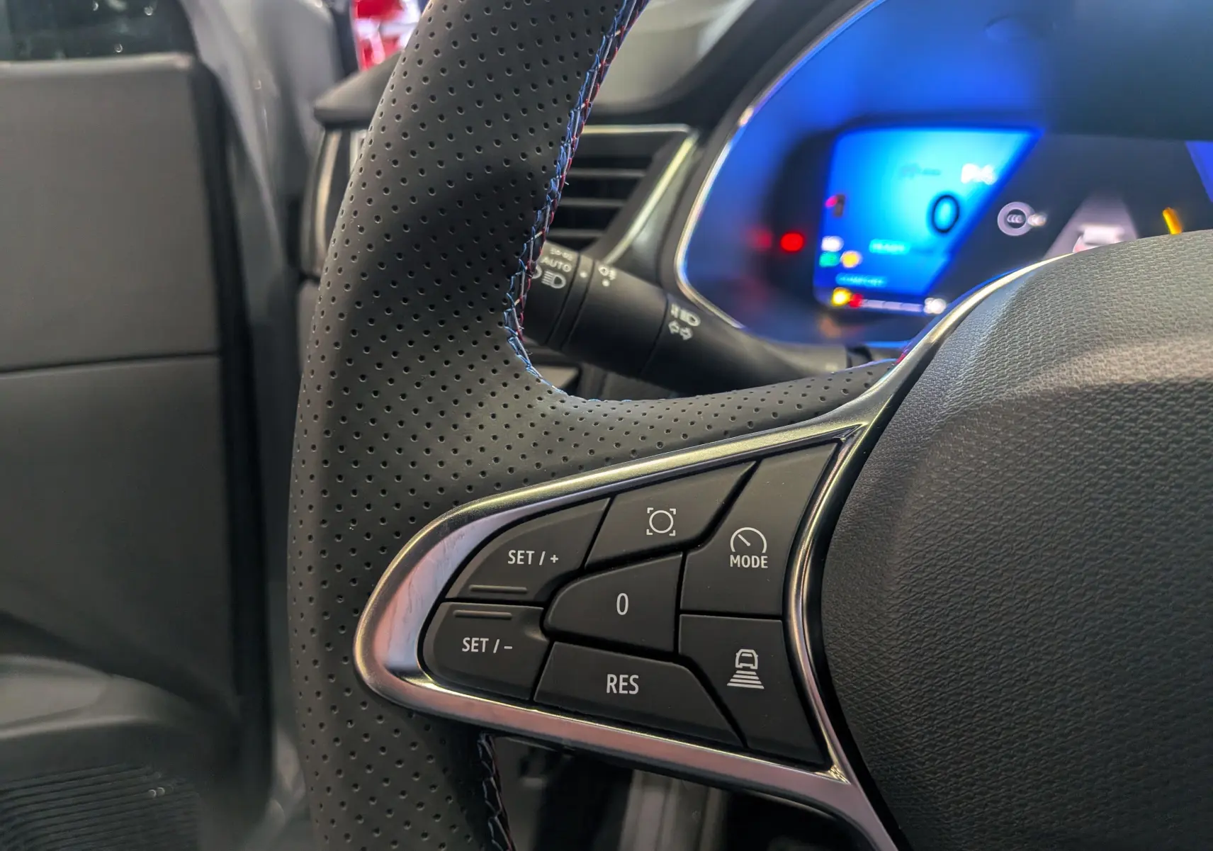 Gros plan sur le volant perforé côté gauche du Renault SYMBIOZ gris, avec commandes de régulateur et tableau de bord numérique bleu.