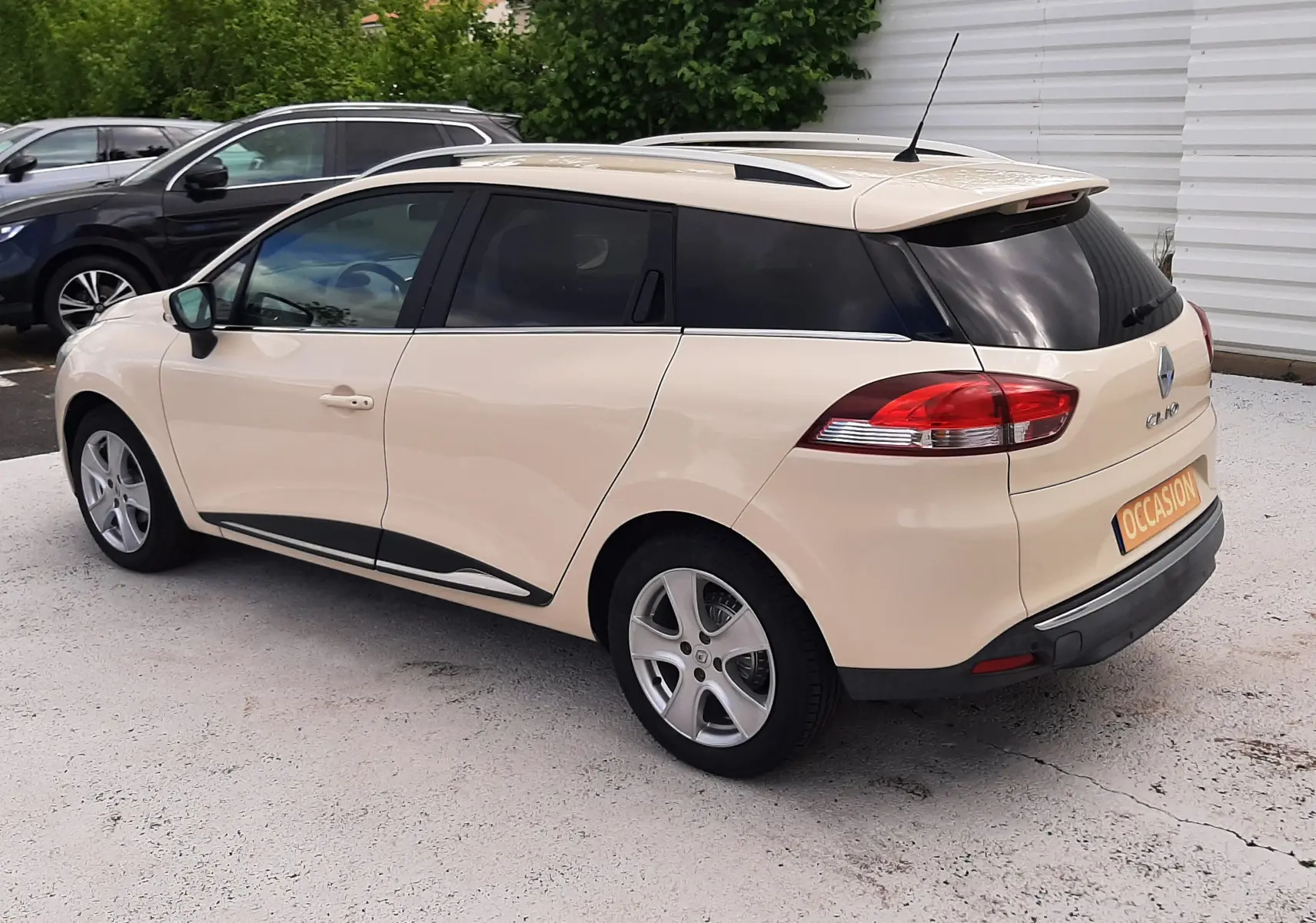 Renault Clio IV Estate beige vue 3/4 arrière droit, avec vitres arrière teintées et jantes alliage 16 pouces.
