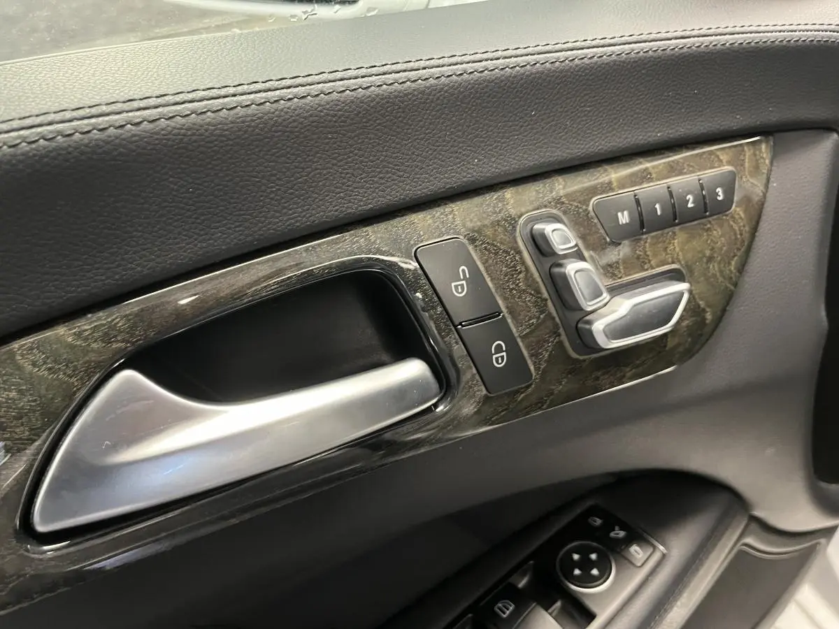 Poignée intérieure côté gauche avec commandes de réglage sièges et mémoire sur panneau en bois foncé d'une Mercedes CLS 350 d gris.
