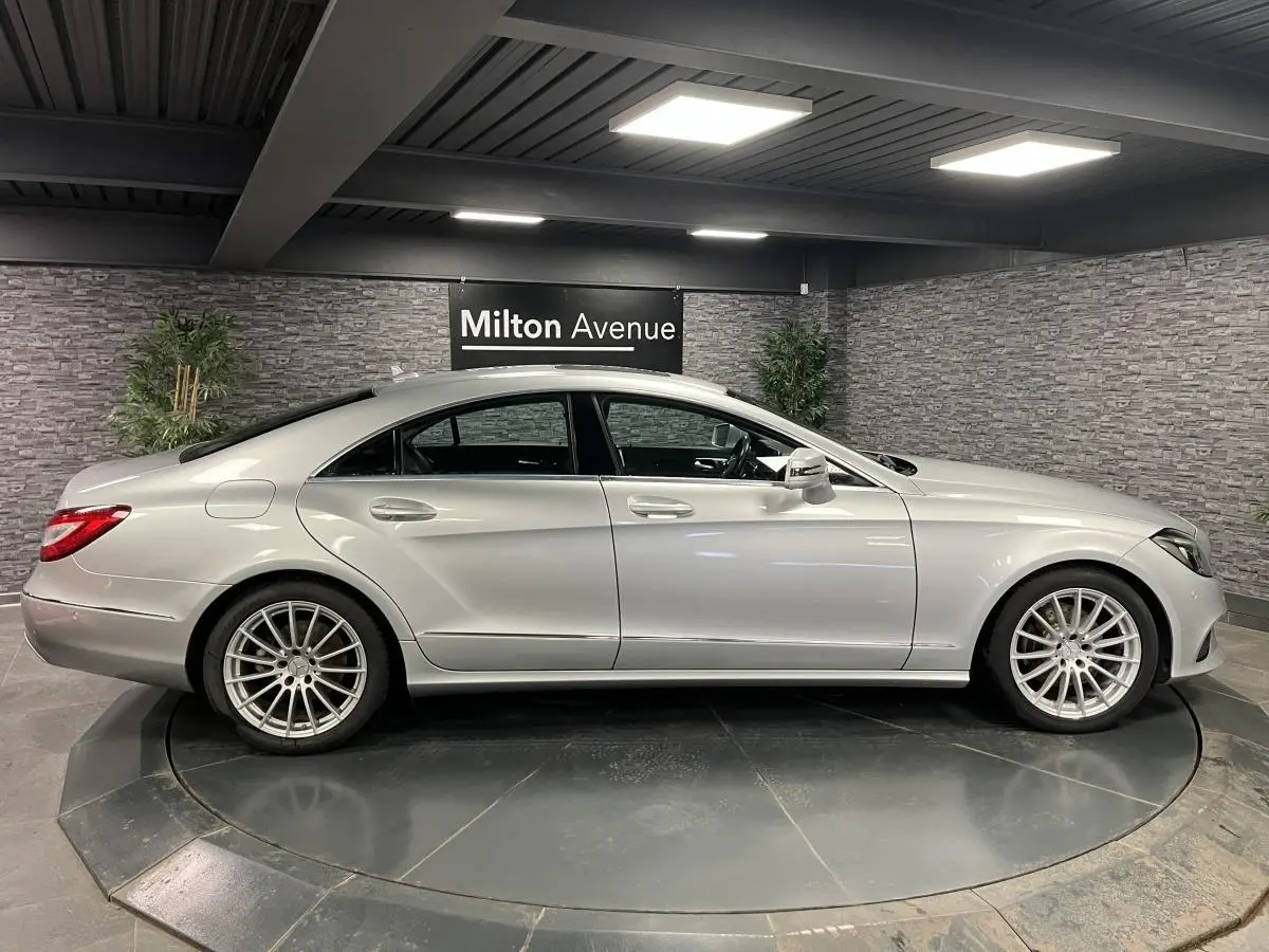 Profil côté gauche d'une Mercedes Classe CLS gris métallisé avec jantes alliage multibranches en showroom.