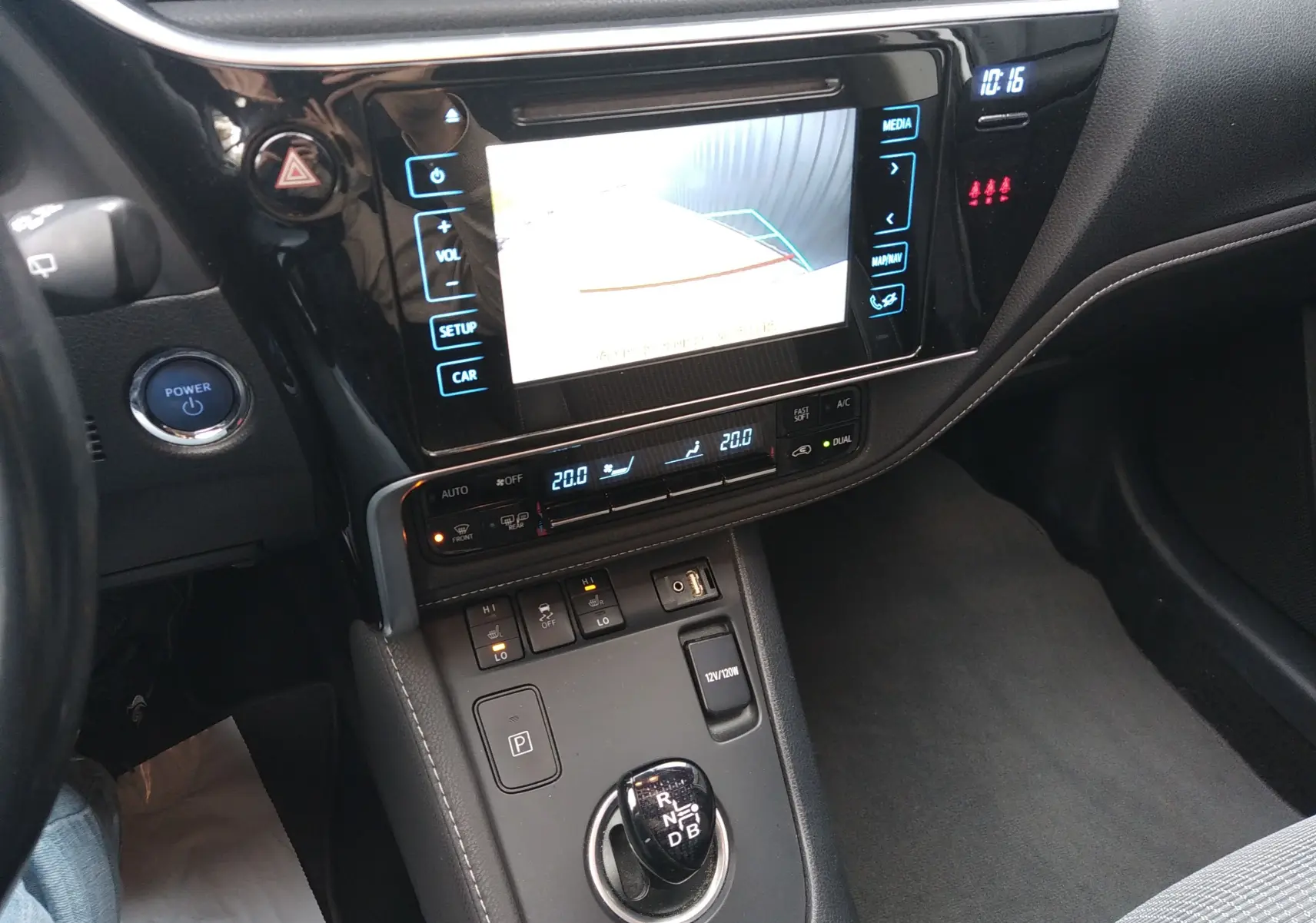 Vue intérieure centrée sur la console centrale et l'écran tactile de la Toyota Auris hybride blanche, avec levier de vitesses automatique.