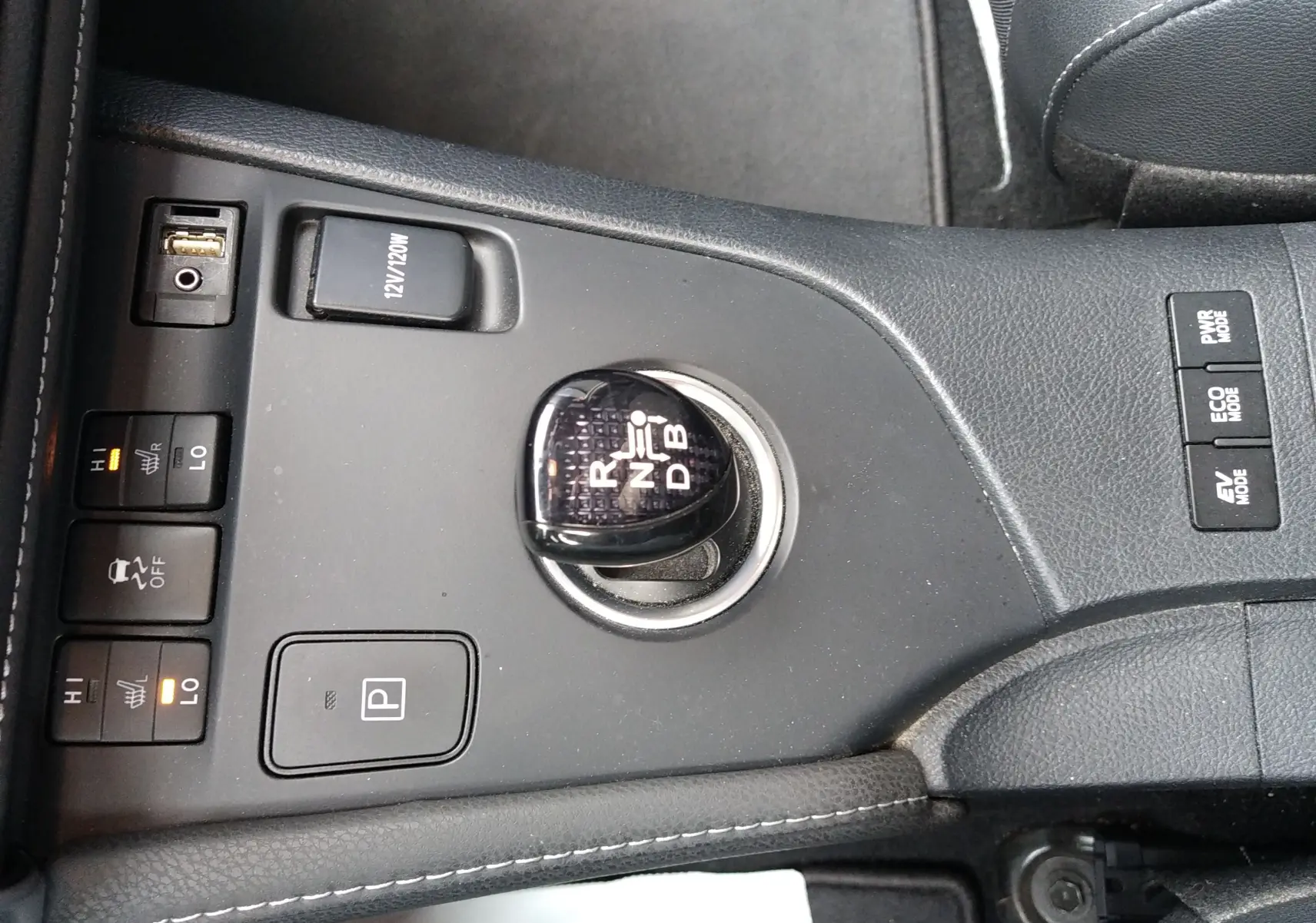 Vue rapprochée de la console centrale noire d’une Toyota Auris hybride 2016, avec levier de vitesses et commandes chauffantes.