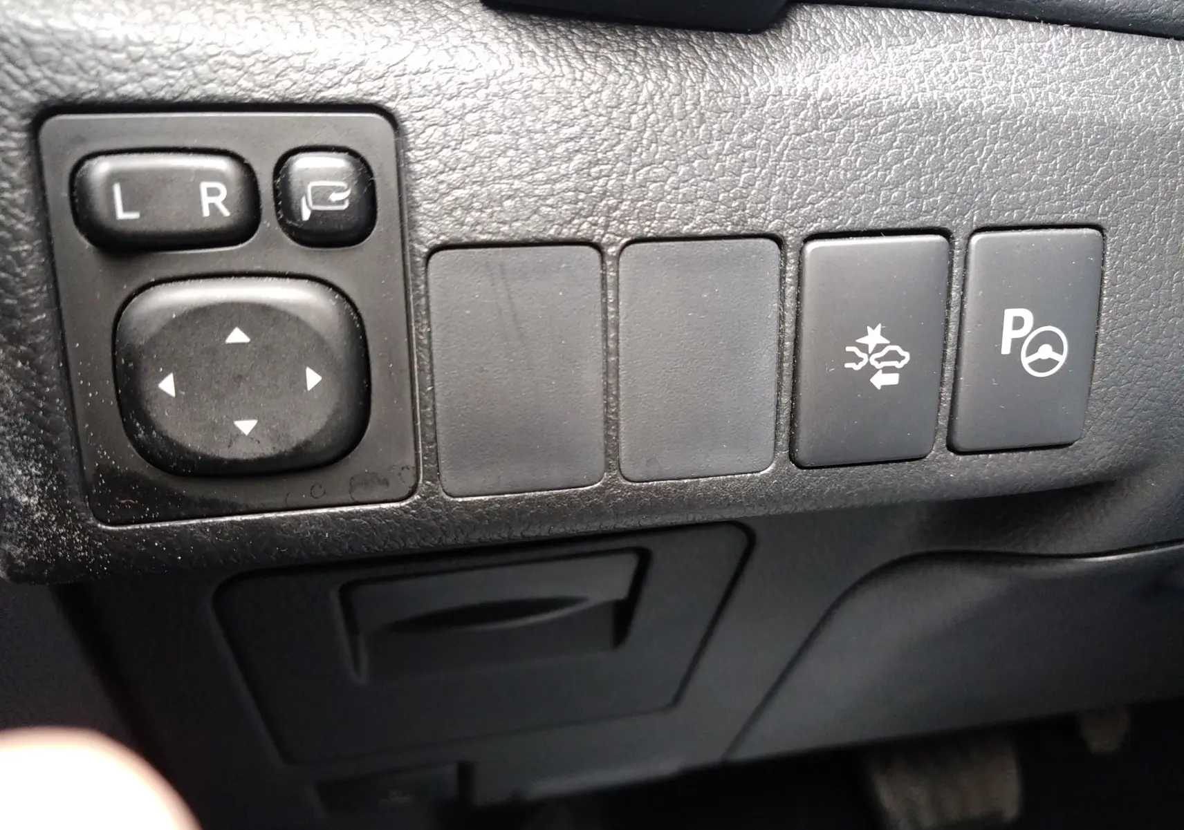 Gros plan sur les commandes de réglage des rétroviseurs et assistance au stationnement dans une Toyota Auris II hybride blanche de 2016.