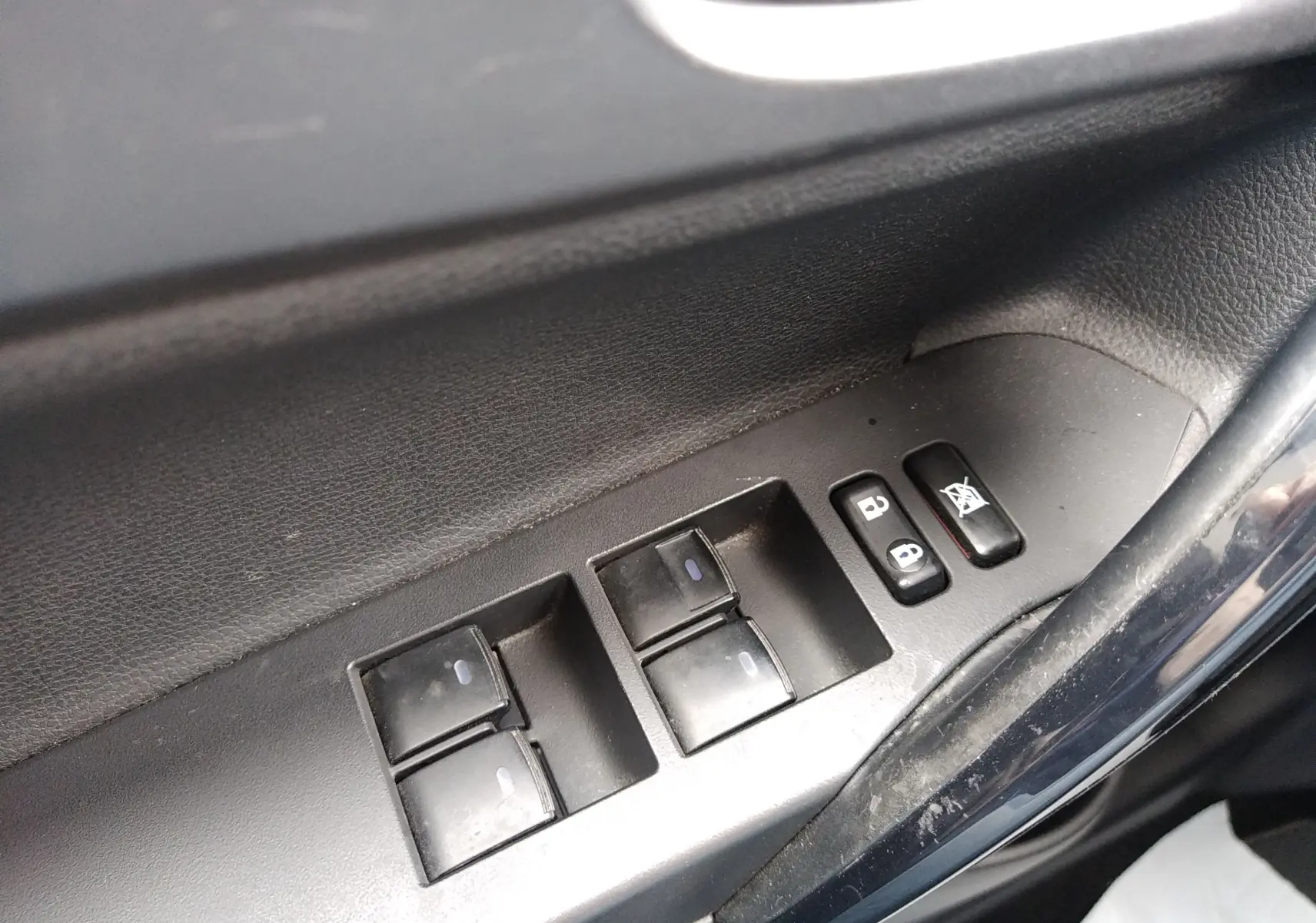 Panneau de commandes des vitres et verrouillage côté conducteur dans l'habitacle d'une Toyota Auris blanche hybride 2016.