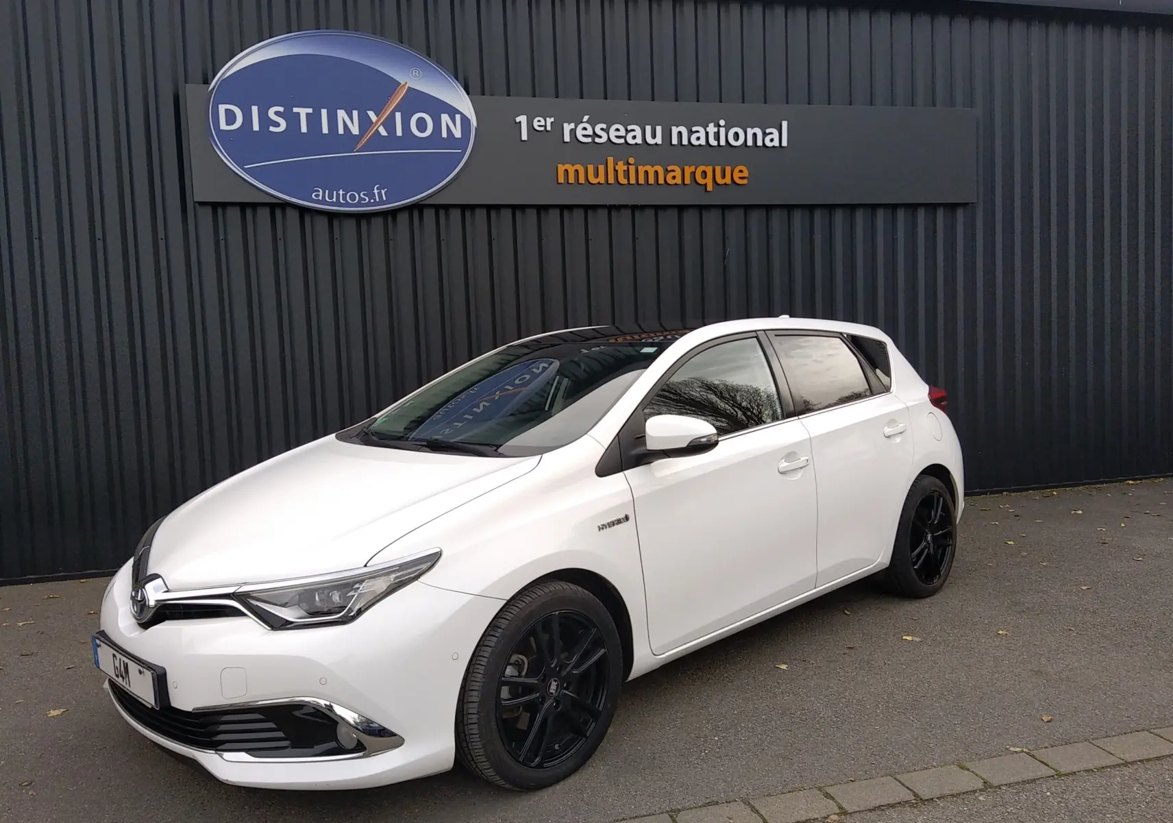 Toyota Auris hybride blanche vue 3/4 avant droit, jantes noires et toit panoramique sombre visible.