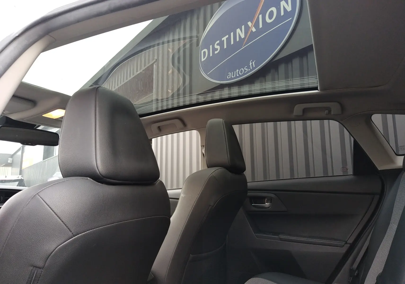 Vue intérieure arrière montrant les sièges avant en cuir noir et le toit panoramique d'une Toyota Auris blanche.