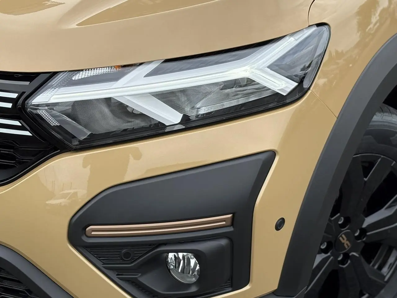 Gros plan sur l'avant droit beige Safari du Dacia Sandero Stepway 2025, avec phares LED et jante noire distinctive.