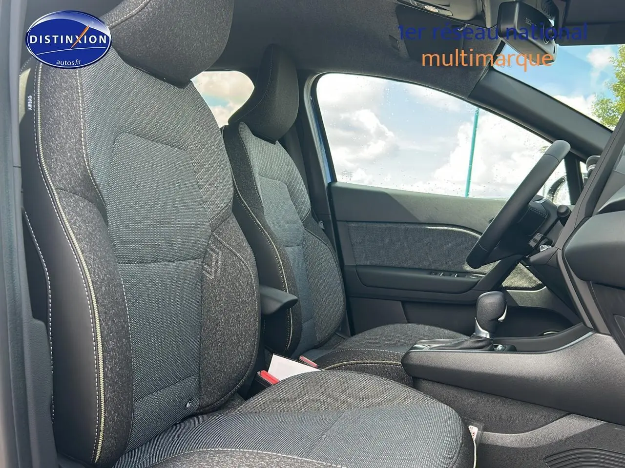 Vue intérieure côté droit du Renault Captur 2025, sièges tissu gris avec accoudoir central et levier de boîte automatique.