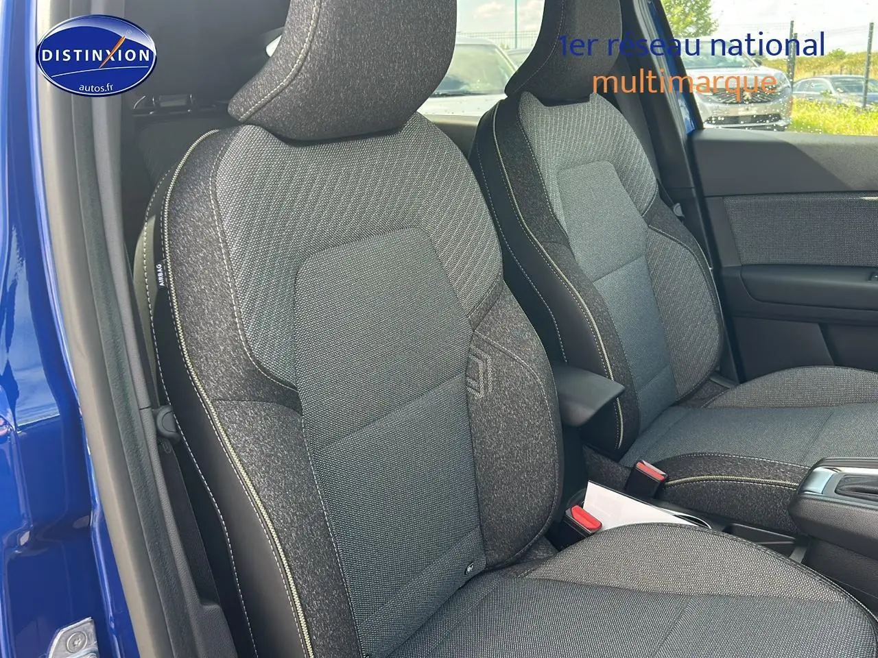 Vue intérieure sur les sièges avant gris du Renault Captur bleu iron, avec accoudoir central et porte ouvert côté gauche.