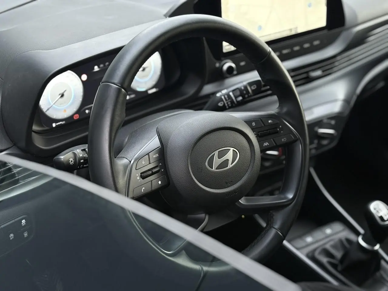 Vue rapprochée du volant cuir noir et du tableau de bord numérique de la Hyundai i20 2025 avec écran tactile GPS.