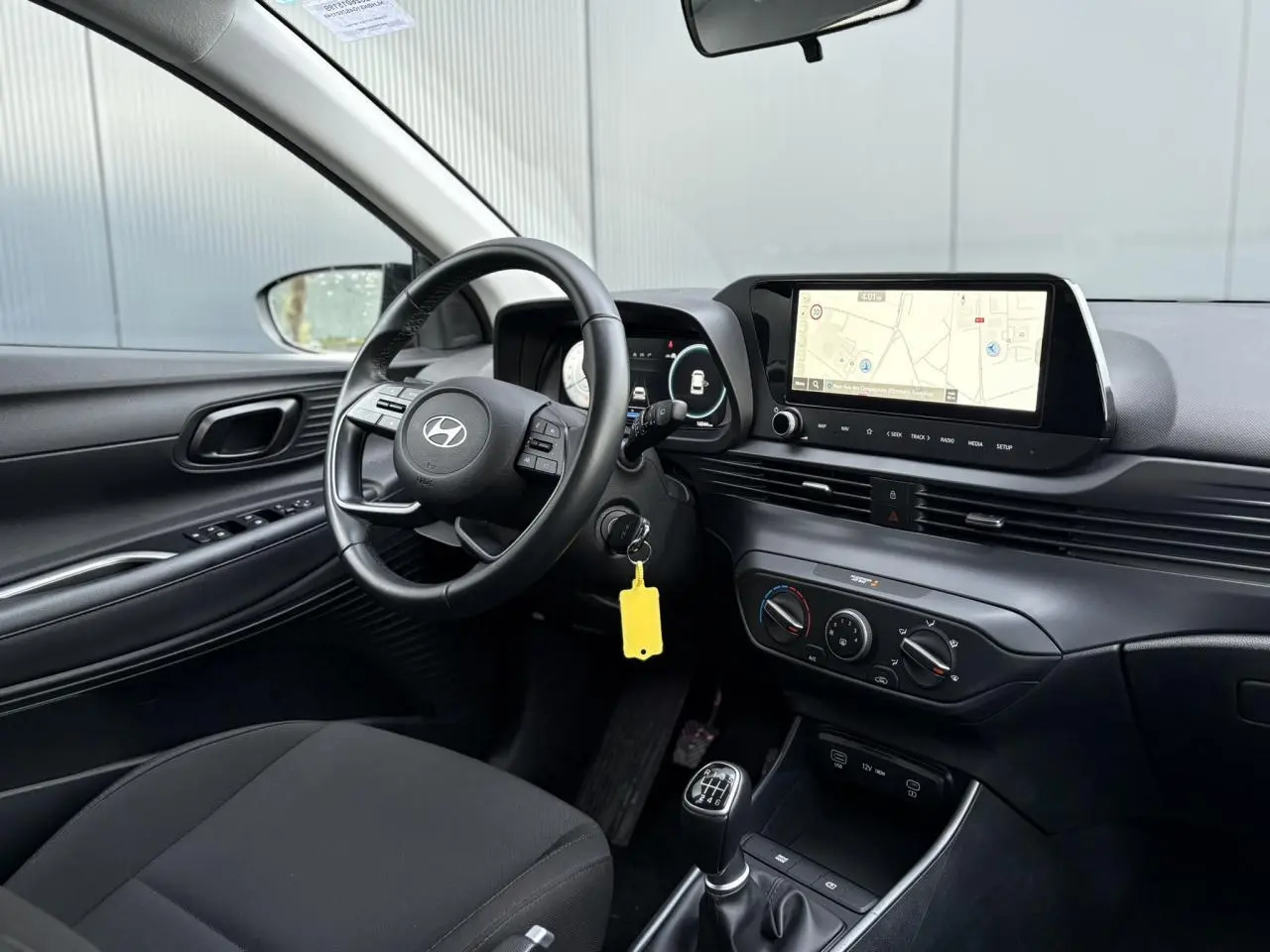 Vue intérieure côté conducteur de la Hyundai i20 2025, volant cuir, écran GPS tactile et levier de vitesses manuel.