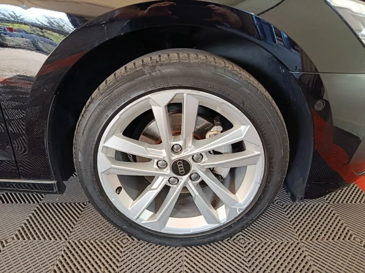 Gros plan sur la roue avant droite d’une Audi A3 noire 2023 avec jante alliage argentée et logo Audi au centre.