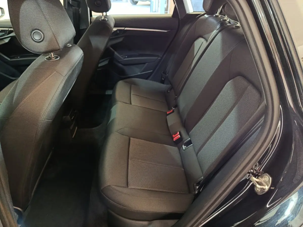 Vue intérieure côté droit sur la banquette arrière noire de l'Audi A3 35 TDI 2023 avec sièges tissu et ceintures rouges.