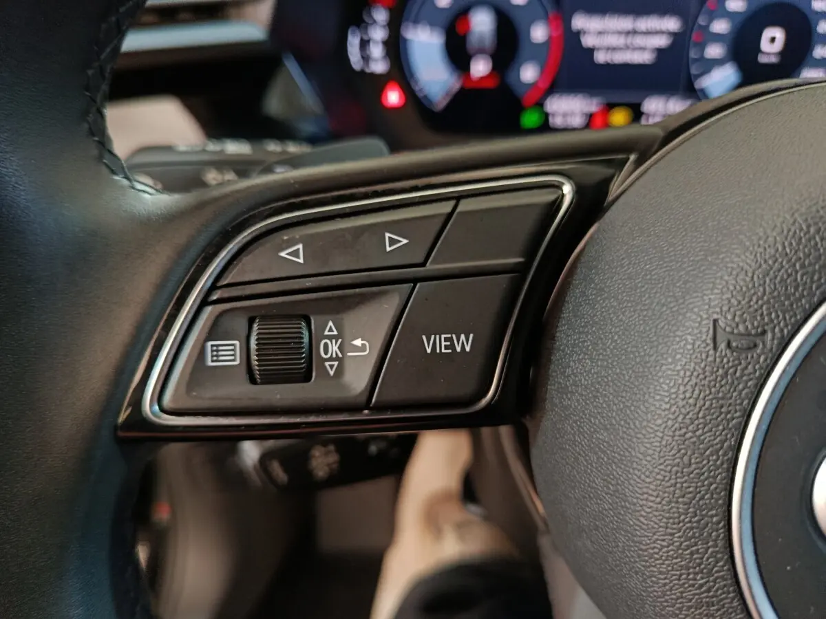 Gros plan sur les commandes gauche du volant cuir noir de l'Audi A3 35 TDI 2023 avec affichage digital en arrière-plan.