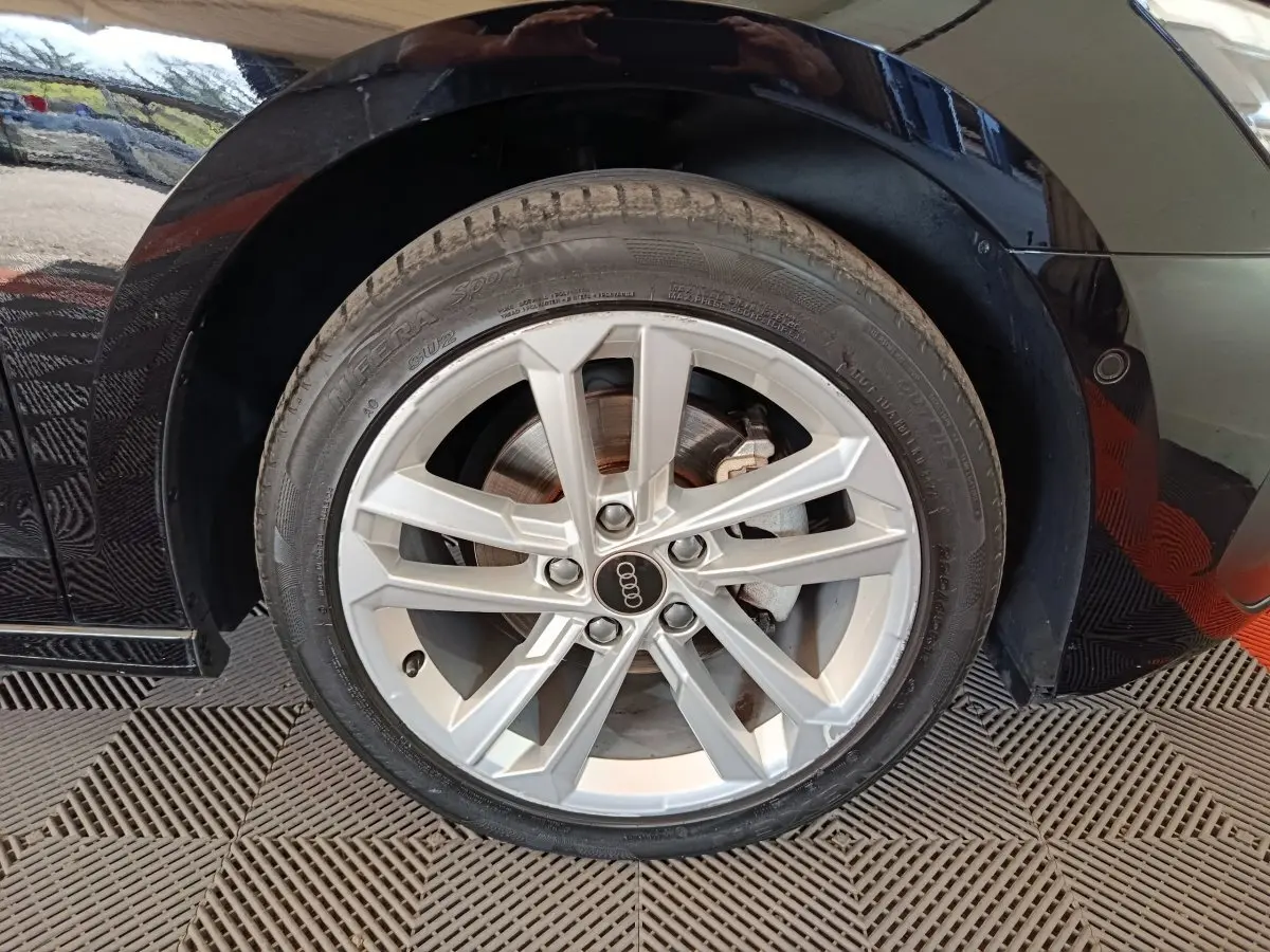 Gros plan sur la roue avant droite d’une Audi A3 noire 2023 avec jante alliage argentée et logo Audi au centre.