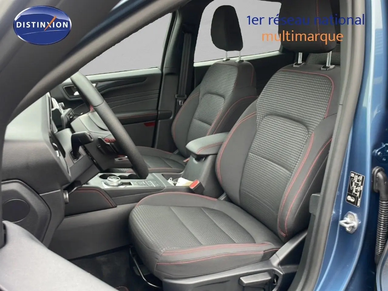 Vue intérieure côté conducteur du Ford Kuga bleu Vapor Metal 2024, sièges tissu noir avec surpiqûres rouges visibles.