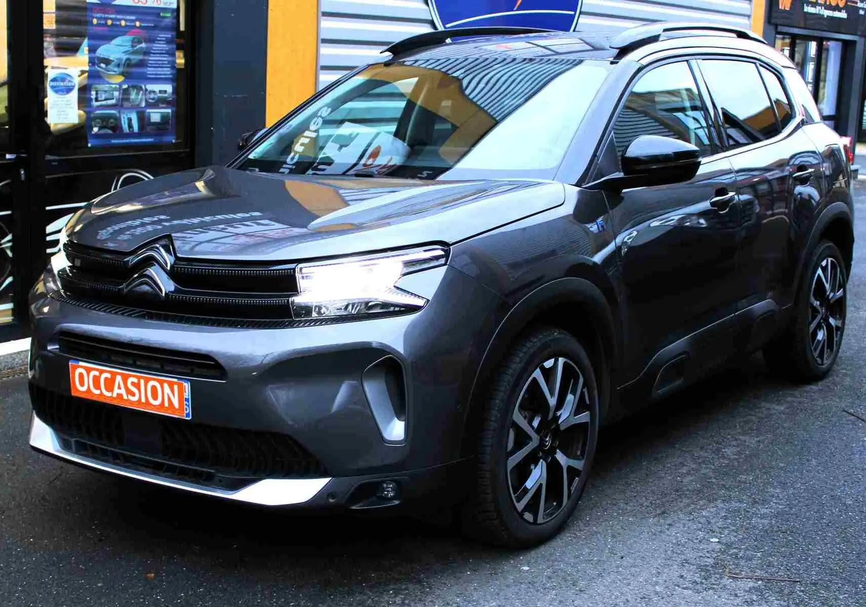 SUV Citroën C5 Aircross gris platinium en 3/4 avant droit, avec jantes noires et phares allumés, affichant un panneau "Occasion".