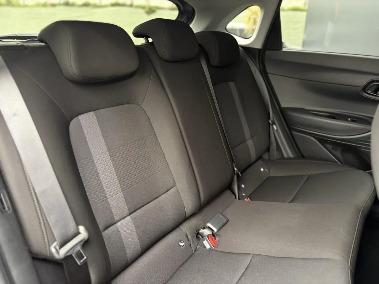 Vue intérieure des sièges arrière noirs de la Hyundai i20 2025, avec ceinture de sécurité et porte latéral visible.