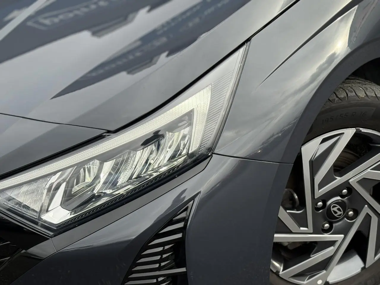 Gros plan sur l'avant droit de la Hyundai i20 2025 gris Aurora Metal, mettant en valeur le phare LED et la jante alliage diamantée.