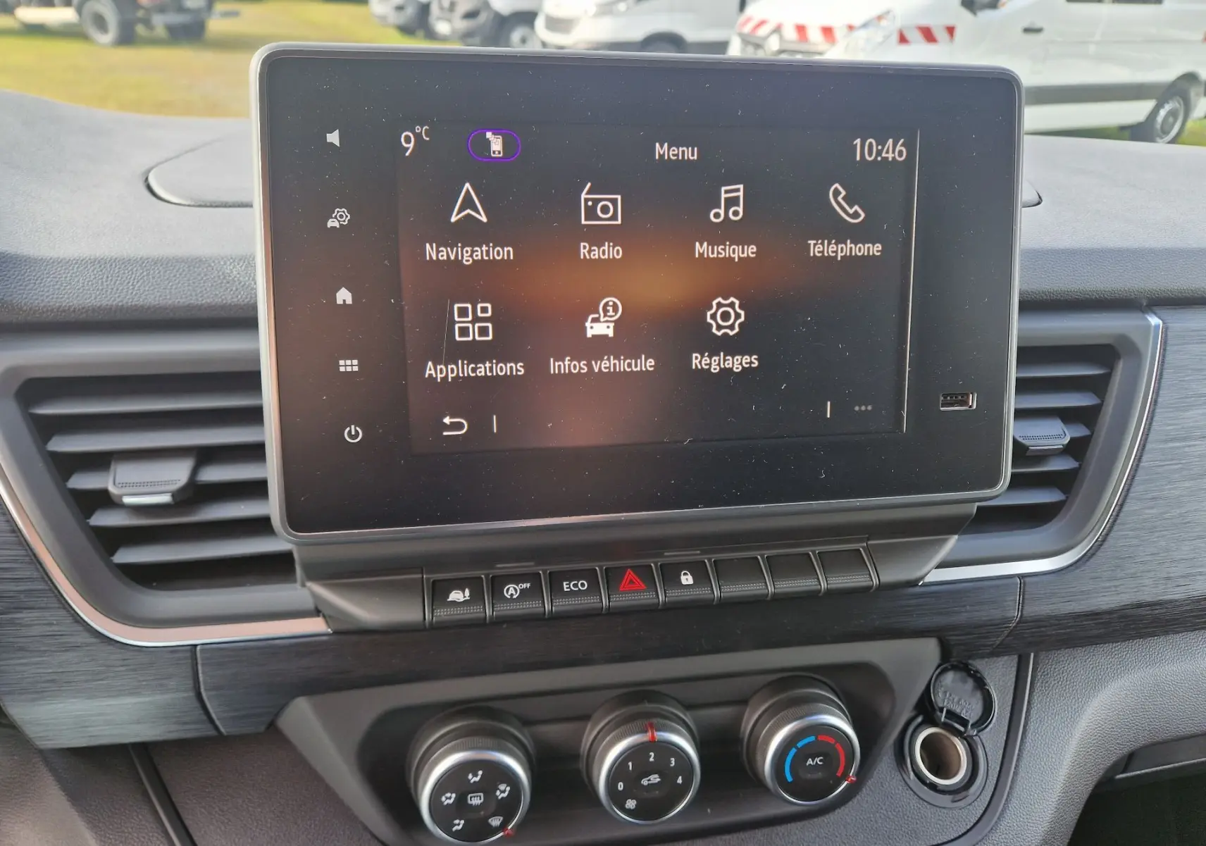 Écran tactile central du tableau de bord du Nissan Primastar 2025 avec commandes climatisation et finition bois visible.
