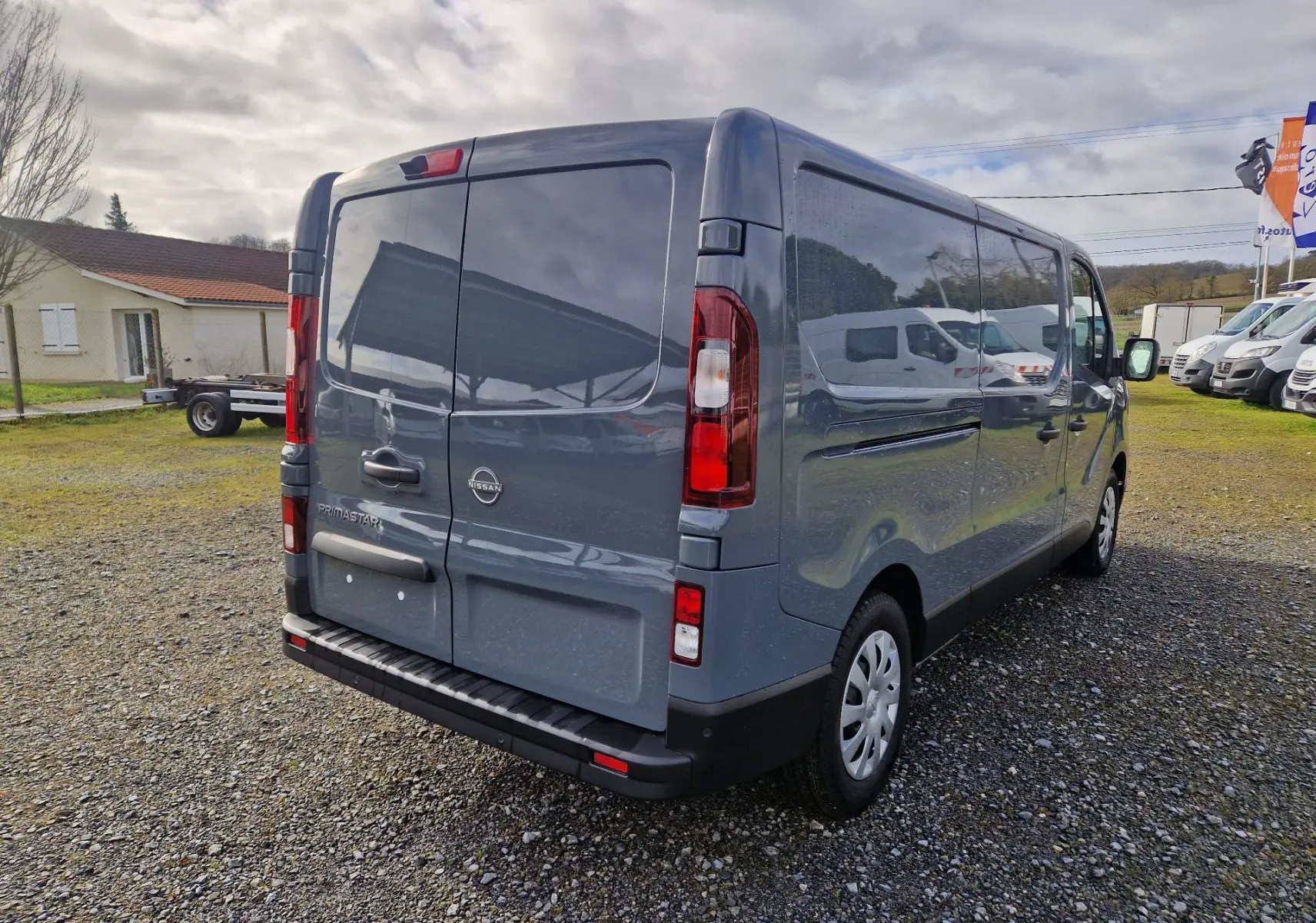 Vue 3/4 arrière droite d’un Nissan Primastar gris urbain 2025 avec portes arrière battantes et vitres teintées.