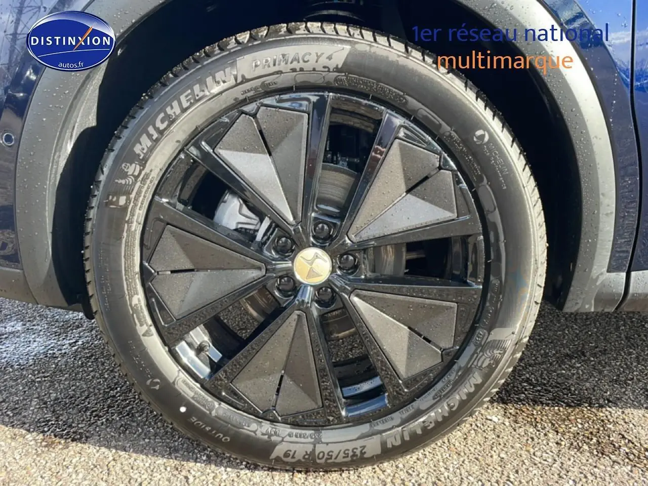 Gros plan sur la roue avant droite d’un DS7 bleu, jante alliage noire au design géométrique distinctif.