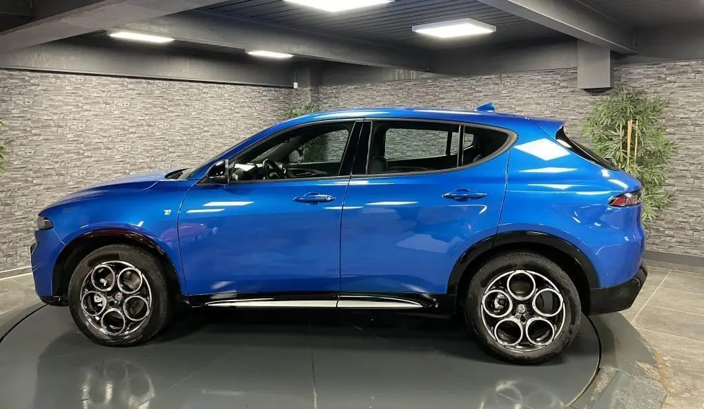 Profil droit de l'Alfa Romeo Tonale 1.5 mHEV 160 TI bleu métallisé avec jantes alliage 18 pouces en intérieur showroom.