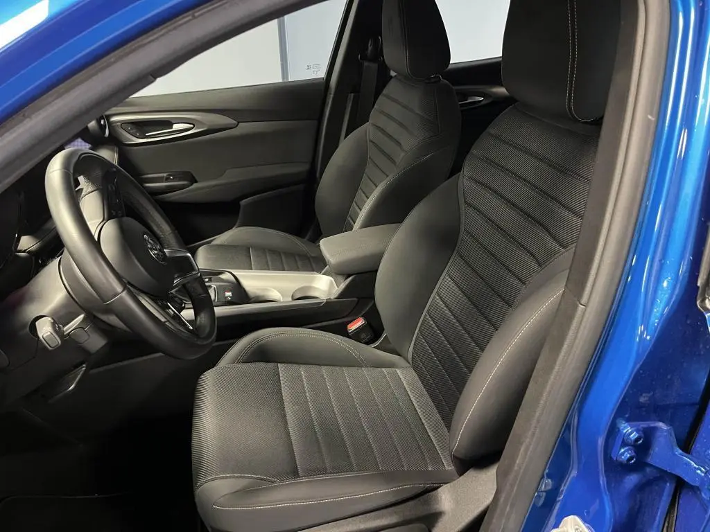 Vue intérieure côté conducteur de l'Alfa Romeo Tonale bleu 2024, sièges AlfaTec noirs avec surpiqûres beige et volant cuir.