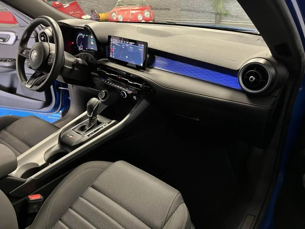 Intérieur avant droit de l'Alfa Romeo Tonale bleu 2024, avec tableau de bord digital et éclairage d'ambiance bleu.