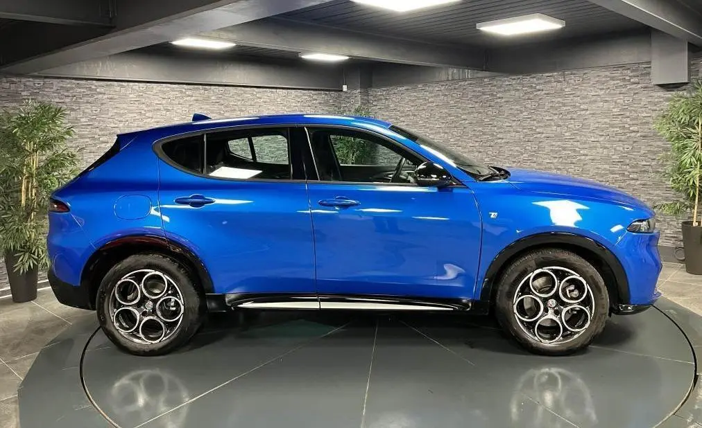 Profil côté gauche de l'Alfa Romeo Tonale 1.5 mHEV 160 TI bleu métallisé avec jantes alliage 18 pouces en intérieur showroom.