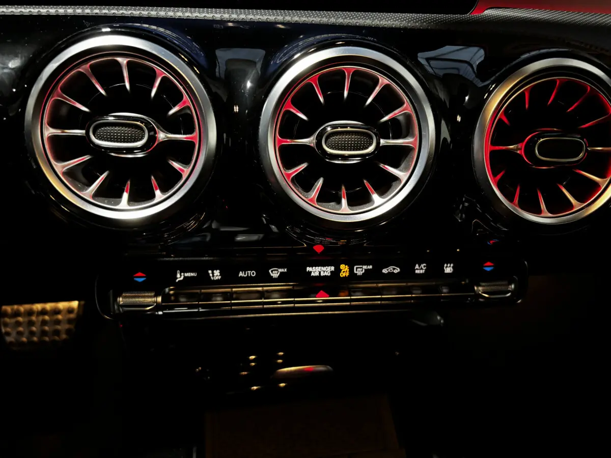 Détail intérieur des aérateurs ronds avec éclairage rouge sur tableau de bord noir de la Mercedes CLA 250 e AMG Line 2023.