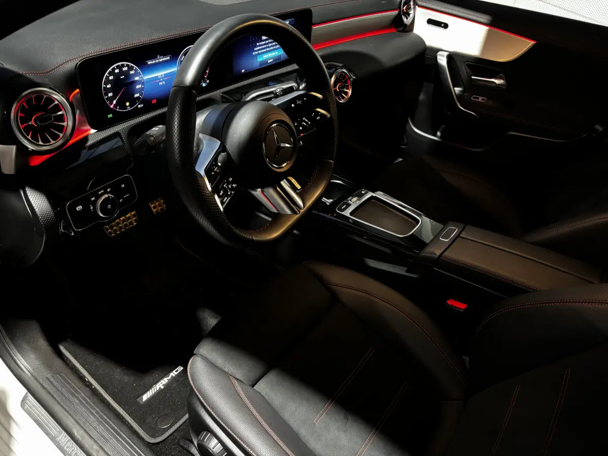 Vue intérieure côté conducteur de la Mercedes CLA 250 e AMG Line 2023, sièges noirs et éclairage d'ambiance rouge.