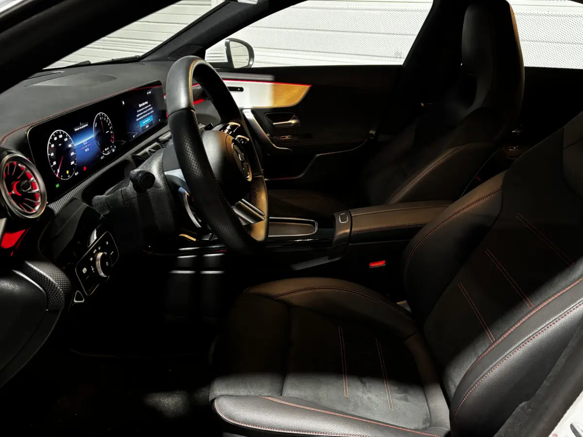 Vue intérieure côté conducteur de la Mercedes CLA 250 e AMG Line 2023, sièges noirs avec surpiqûres rouges et tableau de bord numérique.