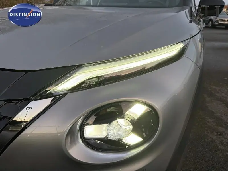 Gros plan sur le phare avant droit allumé du Nissan Juke 1.6 Hybrid 2025 en gris perle métallisé.
