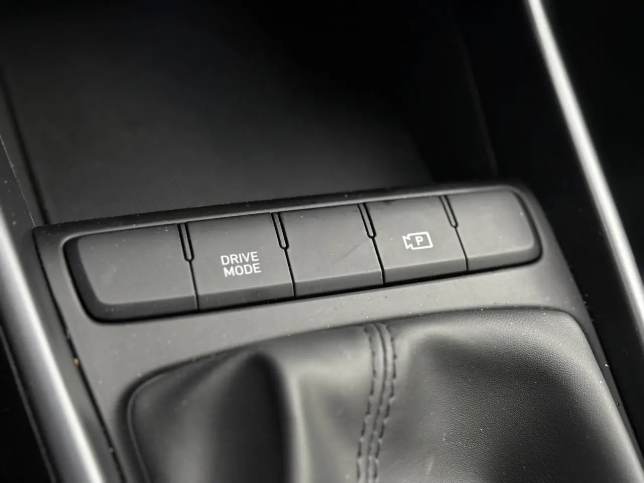 Gros plan sur la console centrale de la Hyundai i20 2025, montrant les boutons Drive Mode et caméra de recul.