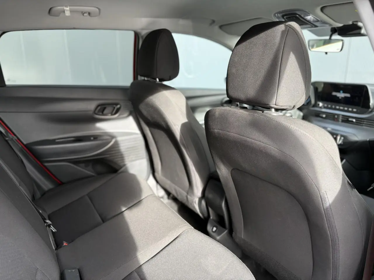 Vue intérieure arrière de la Hyundai i20 rouge Dragon Metal, sièges tissu noirs et tableau de bord avec écran tactile visible.