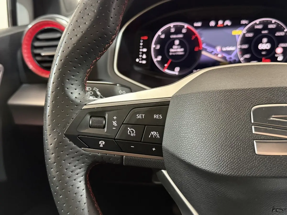 Gros plan sur le volant perforé noir avec surpiqûres rouges de la SEAT Ibiza 2024, tableau de bord numérique en arrière-plan.