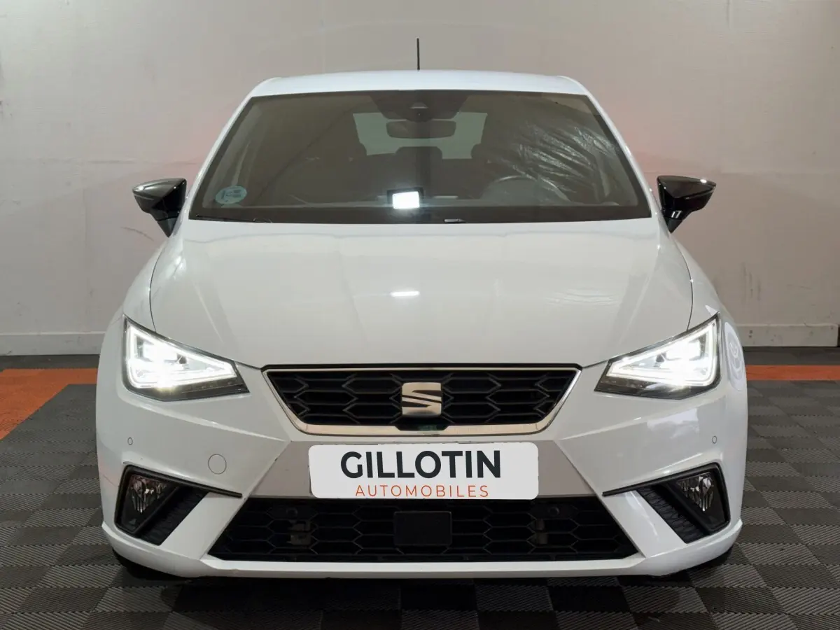 Vue frontale d'une SEAT Ibiza 1.0 TSI 110 FR blanche avec phares LED allumés et calandre hexagonale noire.