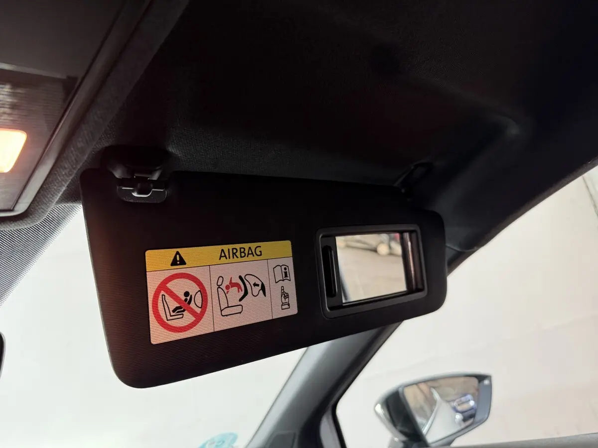 Détail du pare-soleil côté conducteur noir avec miroir intégré et avertissement airbag, rétroviseur extérieur visible.